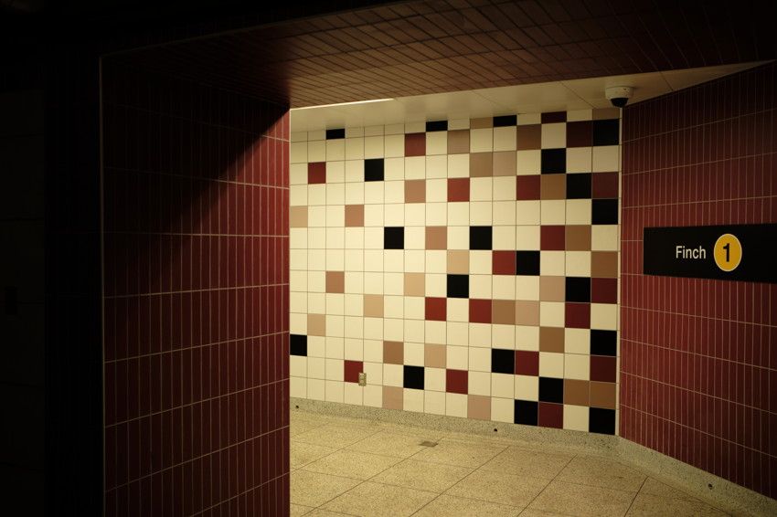Subway corridor: white tiled wall with scattered black, maroon, beige squares; red side tiles and 'Finch 1' sign.