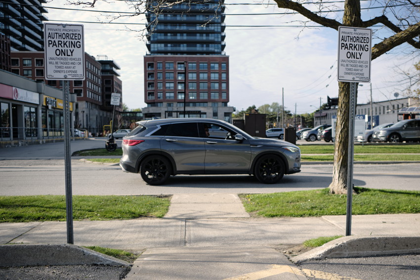 Side view of gray SUV centered between two 'Authorized Parking Only' signs on street, modern apartment building behind.