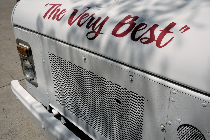 Close-up of a white truck front with red script 'The Very Best', metal grille, headlight, and bumper.