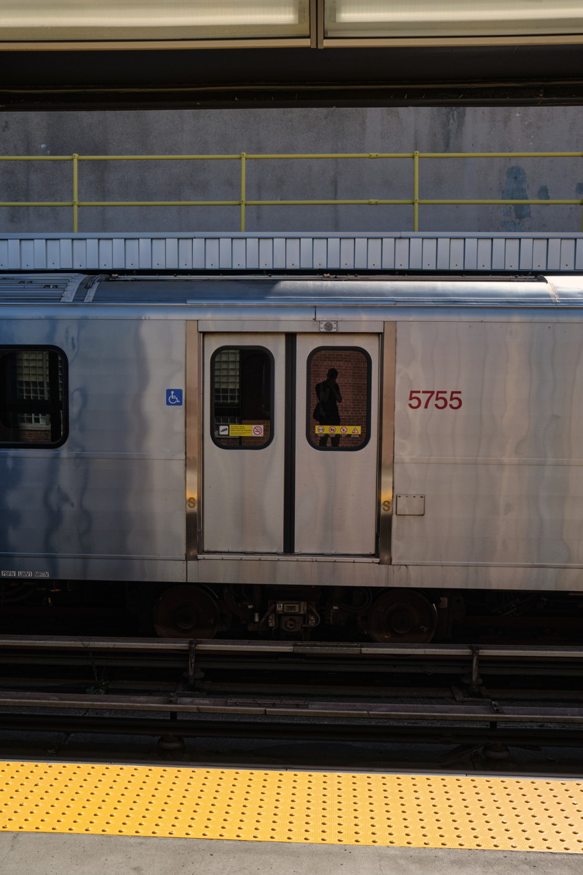 Silver subway car side with closed doors numbered 5755, faint silhouette in window, wheelchair symbol, yellow platform edge.