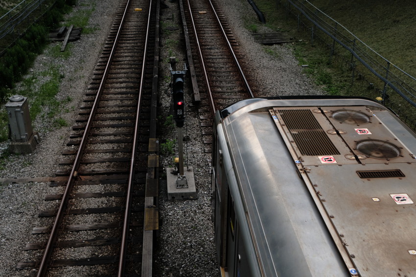 High-angle view of two railway tracks; train roof occupies right side, red signal between tracks.