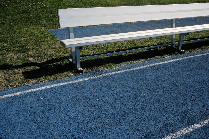 Aluminum bleacher bench beside blue running track with white lane lines and grass behind.