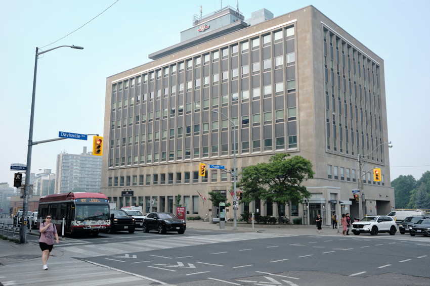 TTC office building at Yonge and Davisville, with a city bus, cars, and pedestrians at the intersection.