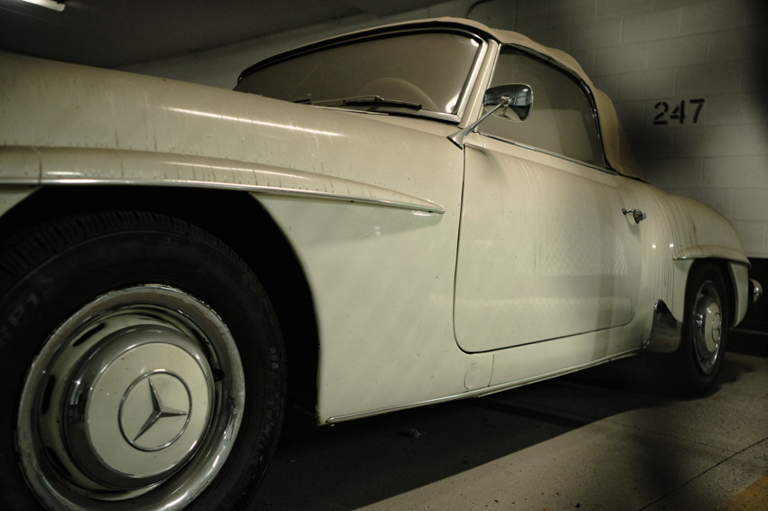 Low-angle view of a white vintage Mercedes-Benz coupe parked in a garage beside space number 247.