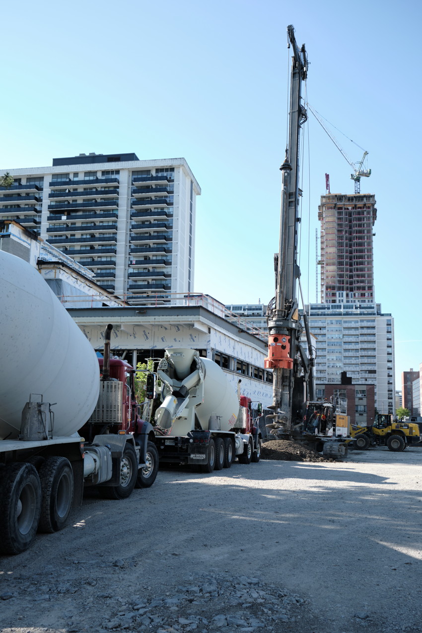 Construction site with concrete mixer trucks, drilling rig, and high-rise buildings under construction.
