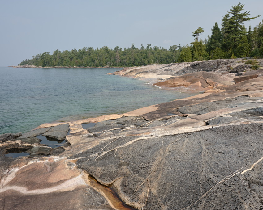 Pink-gray granite shoreline with tidal pools, clear turquoise water, and forested headland.