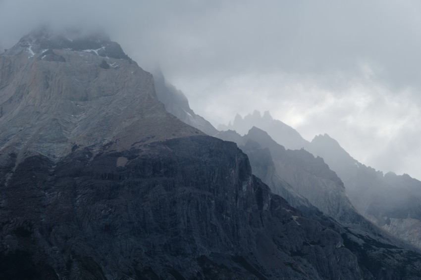 Fog-shrouded layered mountain peaks and steep rocky cliffs under overcast sky.