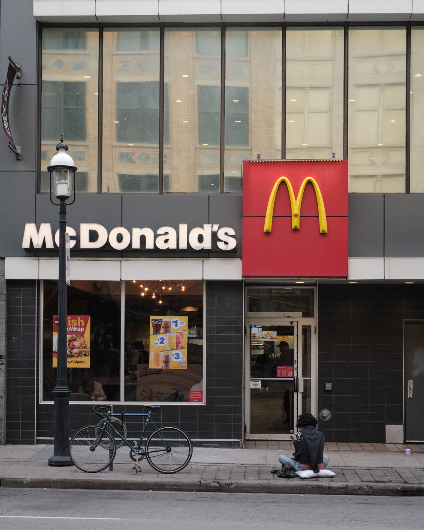 McDonald's storefront with large golden arches, glass windows, bicycle locked to lamppost, person seated on sidewalk.