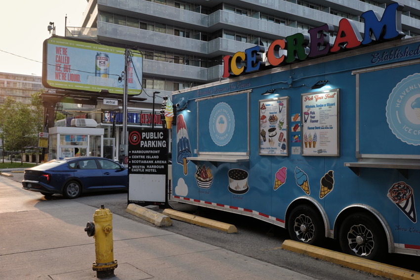 Blue ice cream trailer at curb with signage; yellow fire hydrant foreground, car and apartments behind.