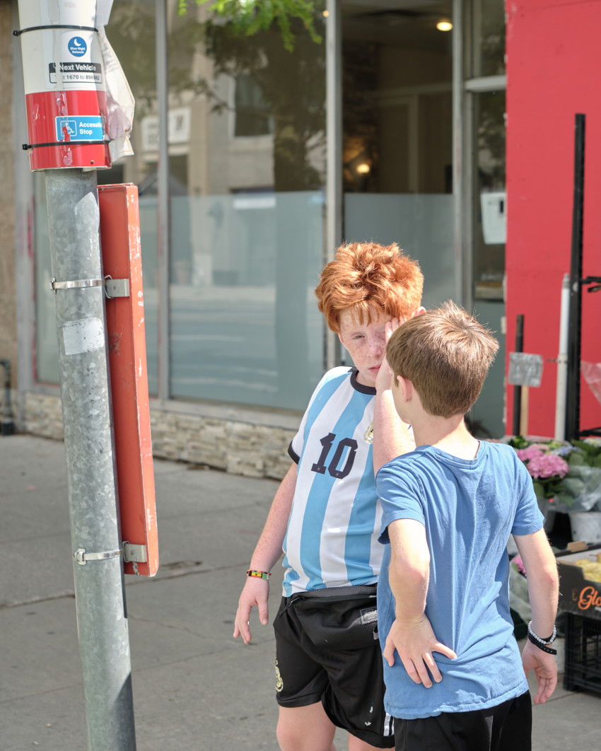 Two boys talking on sidewalk; red-haired boy in striped #10 soccer shirt and a boy in blue T-shirt.