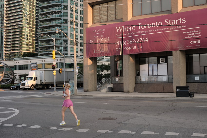 Runner crossing city intersection; office building with large maroon 'Where Toronto Starts' banner.